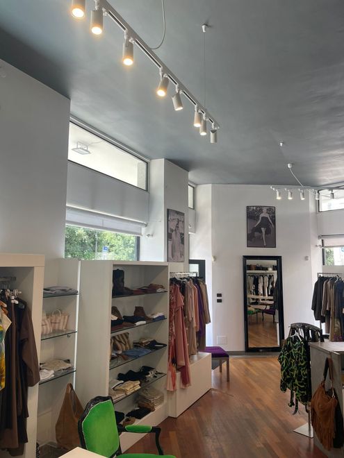 Luminosa boutique di abbigliamento con scaffali bianchi, lampade a sospensione, pavimento in legno e appendiabiti.