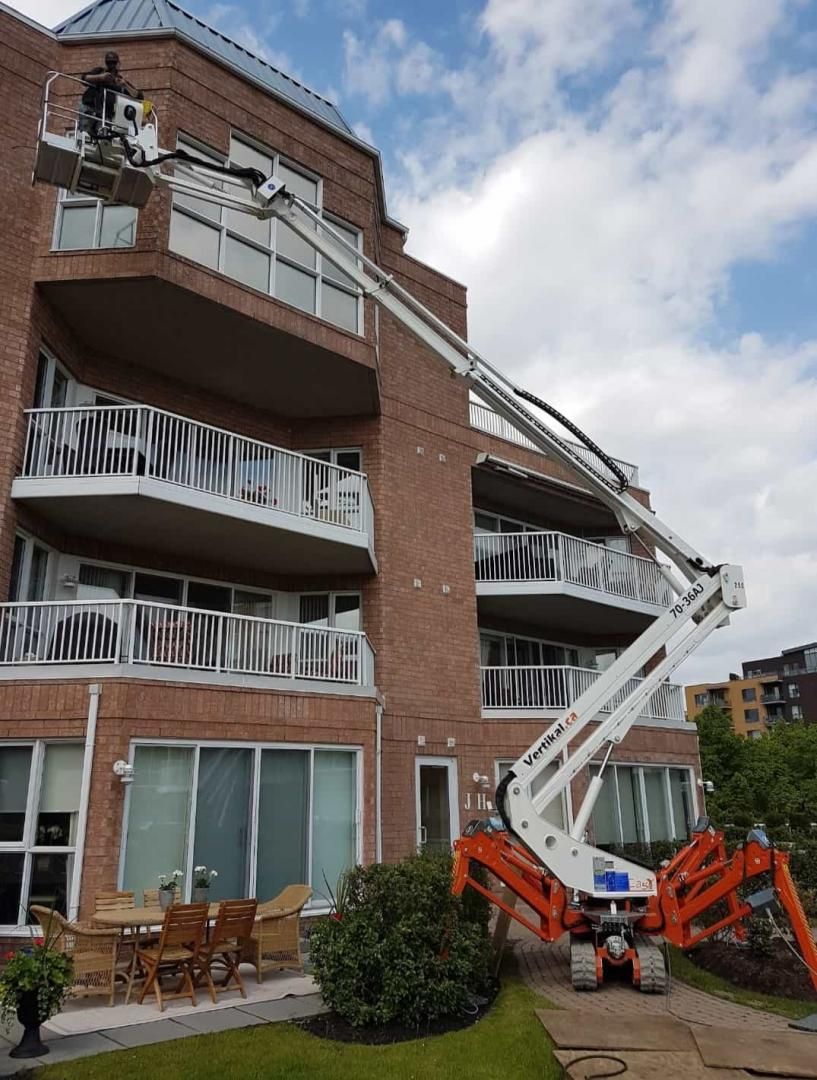 Un ascenseur articulé blanc et orange permet d'accéder à un bâtiment en briques ; il est utilisé pour les réparations.