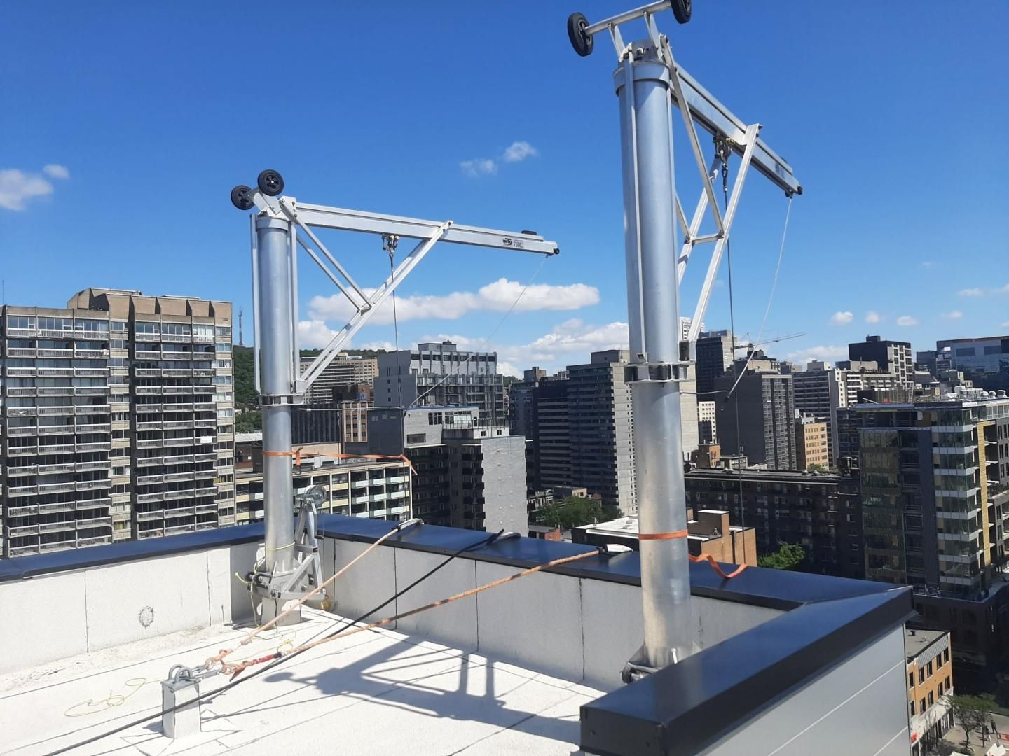 Deux bras de bossoir argentés fixés sur le toit d'un immeuble. Ciel bleu, autres bâtiments en arrière-plan.