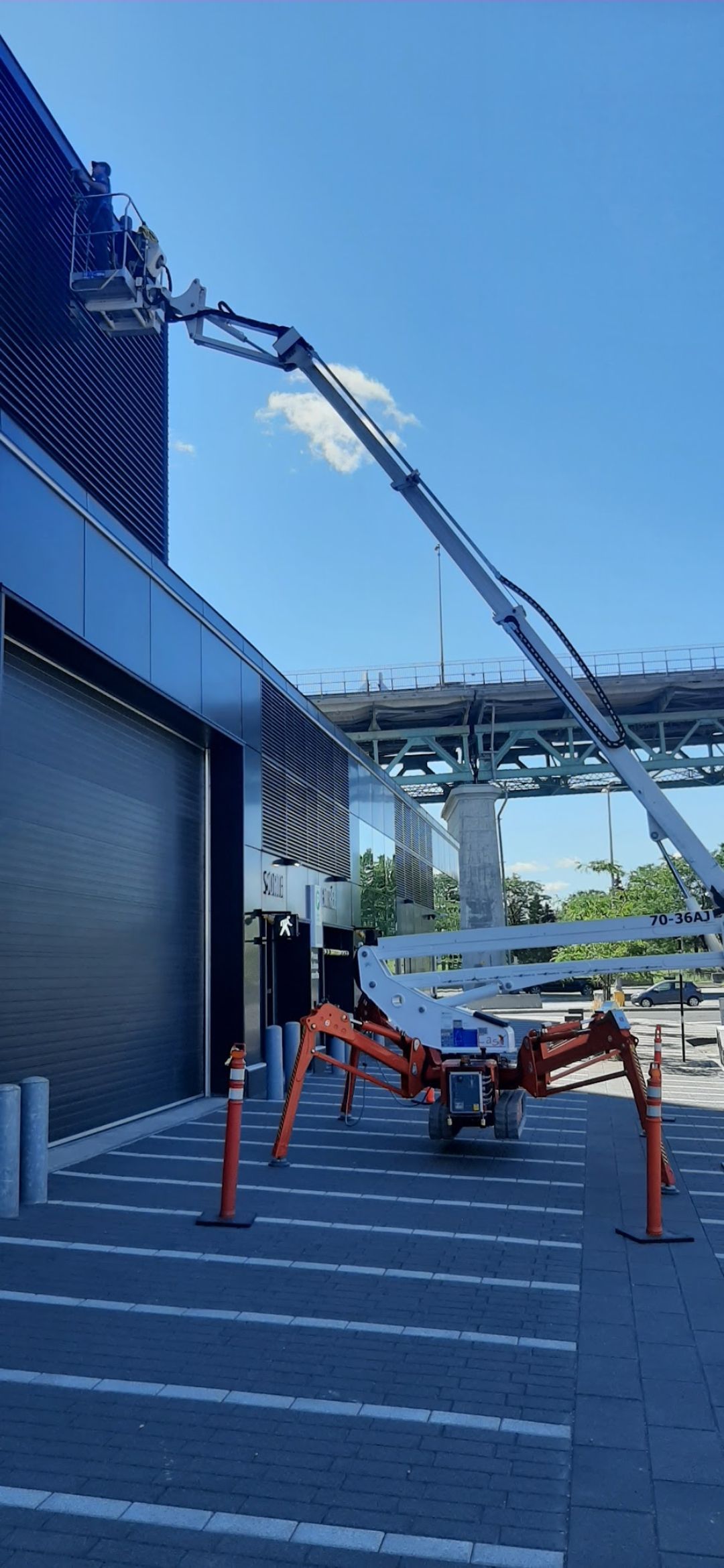 Un ascenseur araignée orange se déploie sur le côté d'un bâtiment sous un ciel bleu.