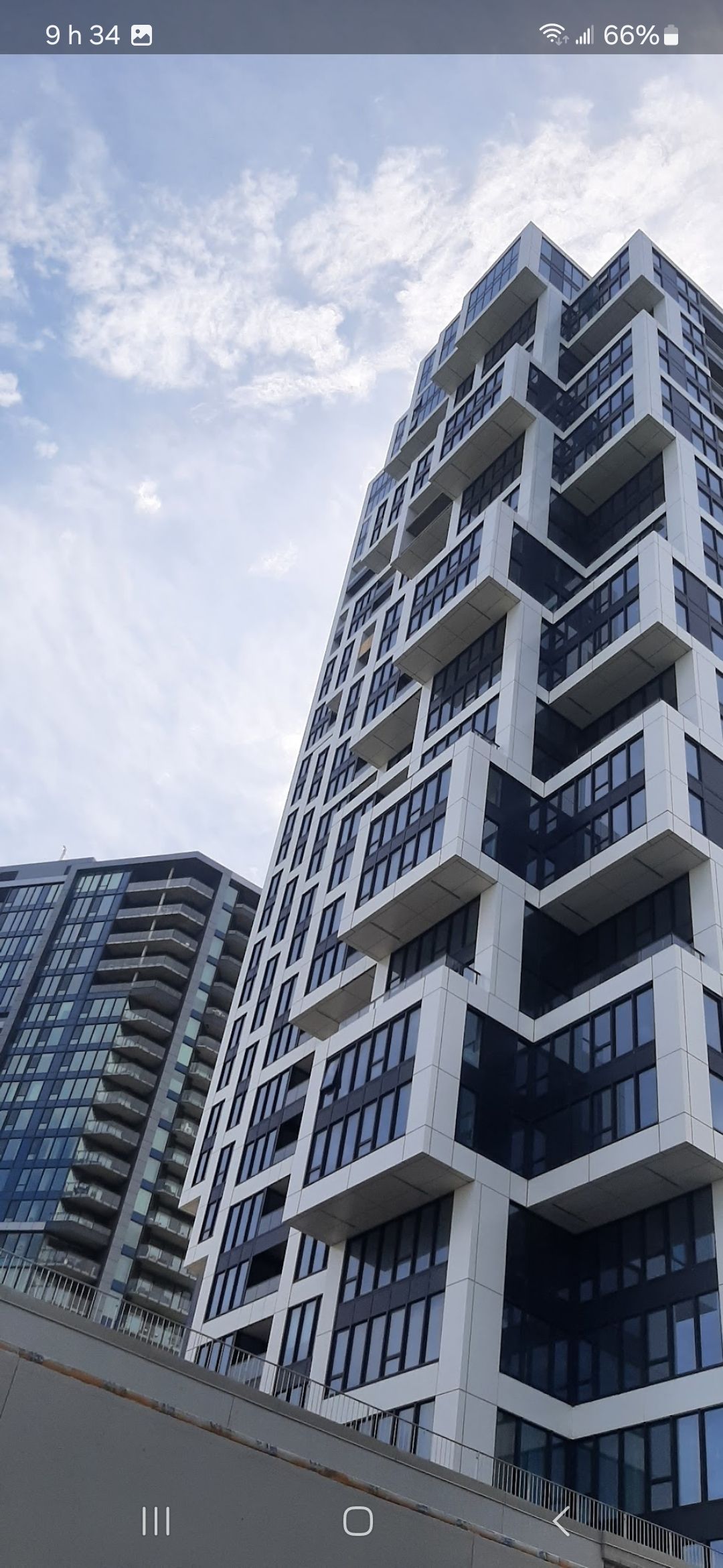 Des immeubles modernes de grande hauteur, aux façades blanches et noires, se détachent sur un ciel nuageux.