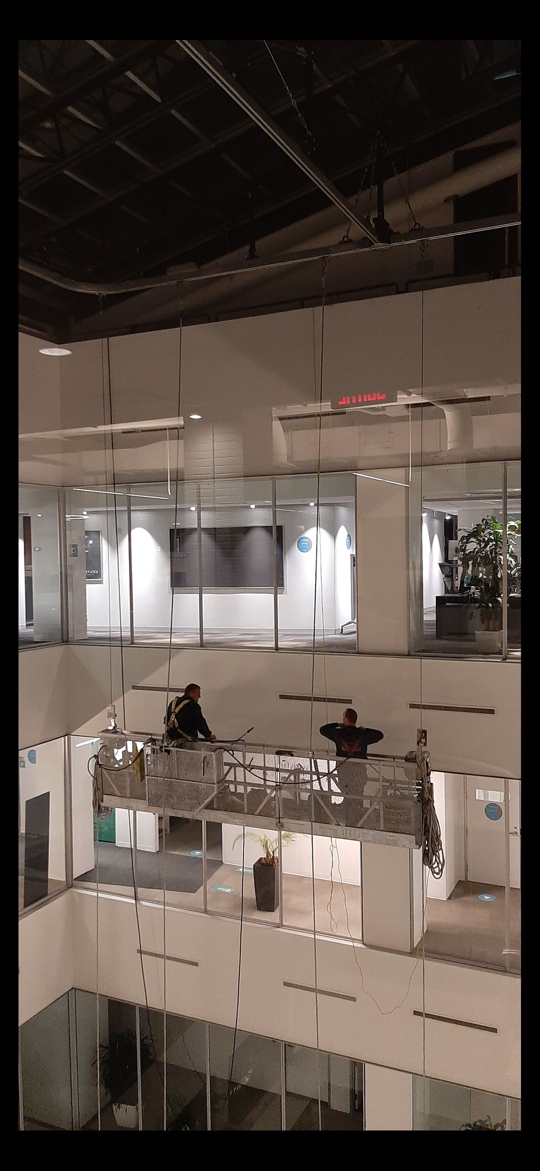 Des ouvriers sur une plateforme surélevée à l'intérieur d'un immeuble de bureaux à plusieurs étages.