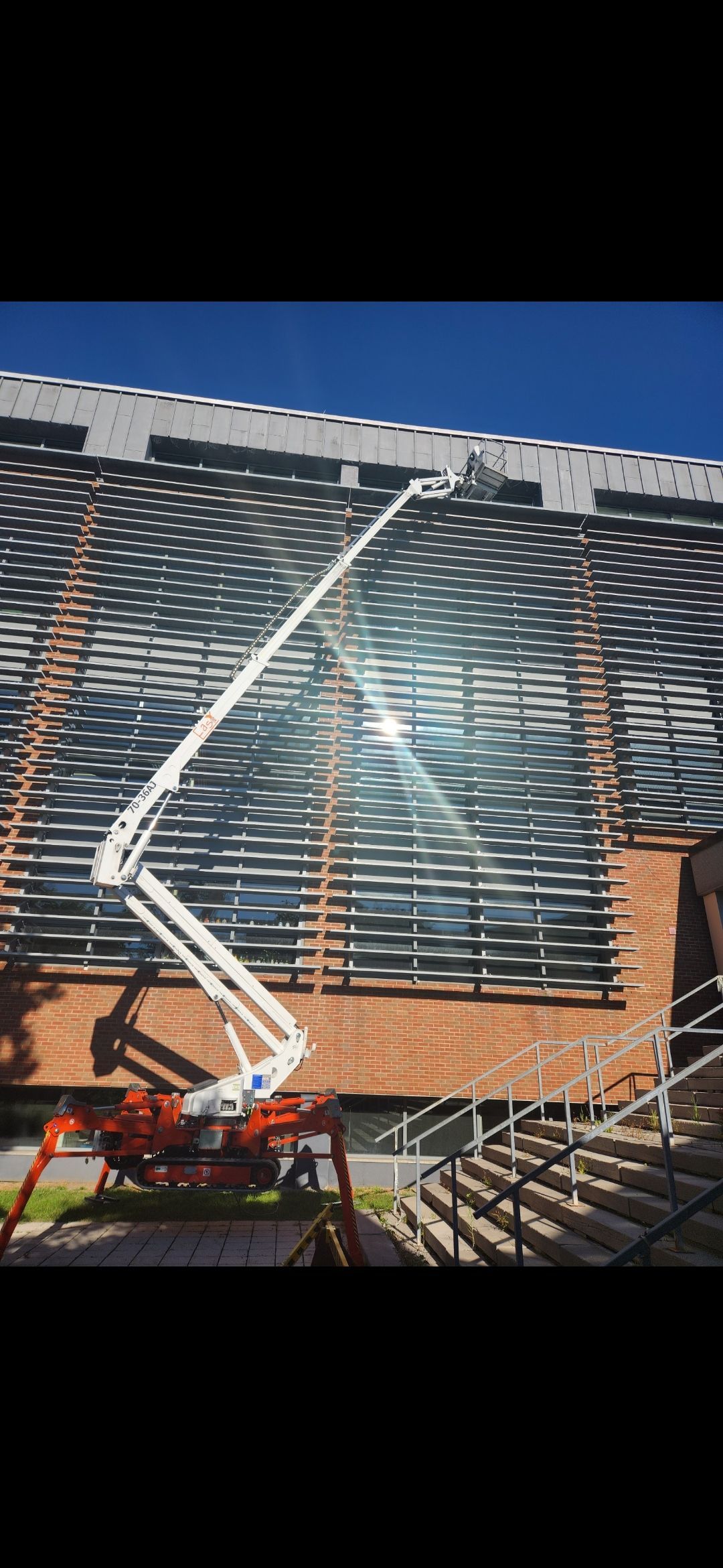 Une nacelle élévatrice blanche travaille sur la structure métallique d'un bâtiment sous un ciel bleu.