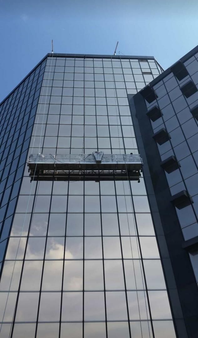 Immeuble de grande hauteur aux façades de verre, doté d'une plateforme suspendue pour le lavage des vitres, se détachant sur un ciel bleu azur.