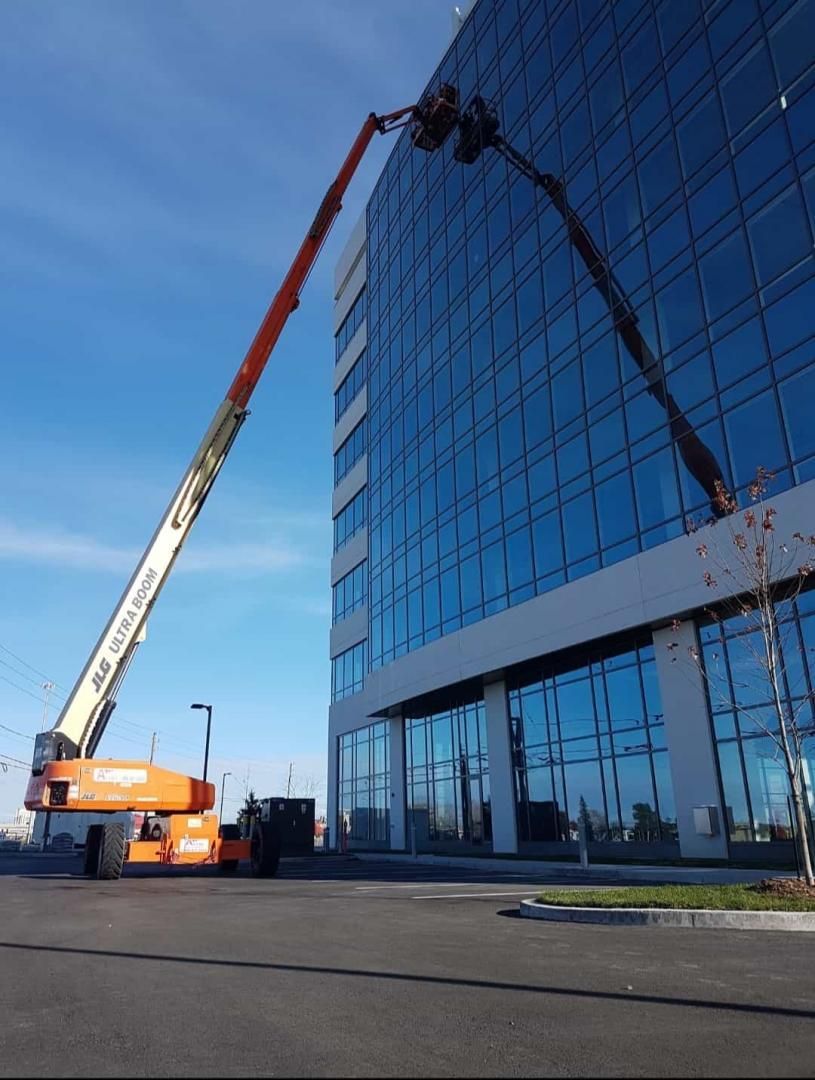 Deux nacelles élévatrices orange et blanches se dirigent vers un bâtiment en verre par une journée ensoleillée.