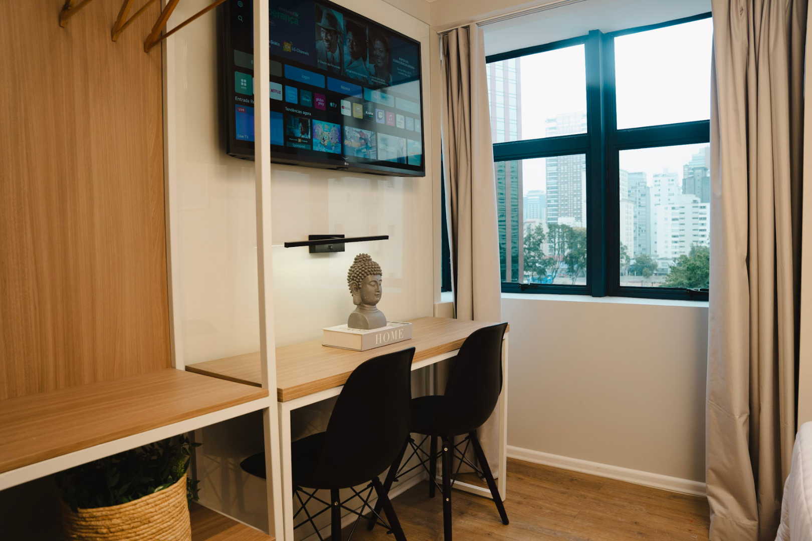 Escritório moderno em casa com mesa, cadeira, TV de parede e janela grande com cortinas.
