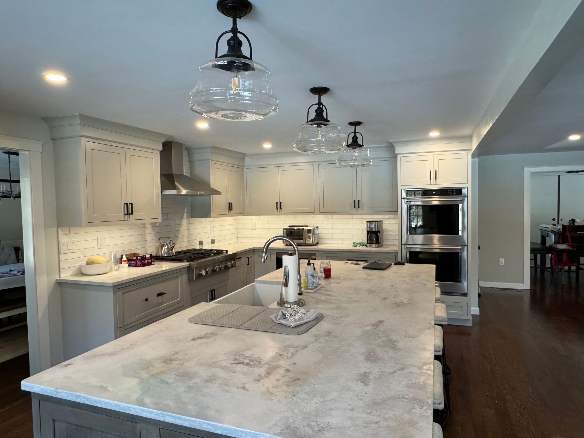 A bright, modern kitchen with light grey cabinetry, a large marble-topped island, stainless appliances, and pendant lights.