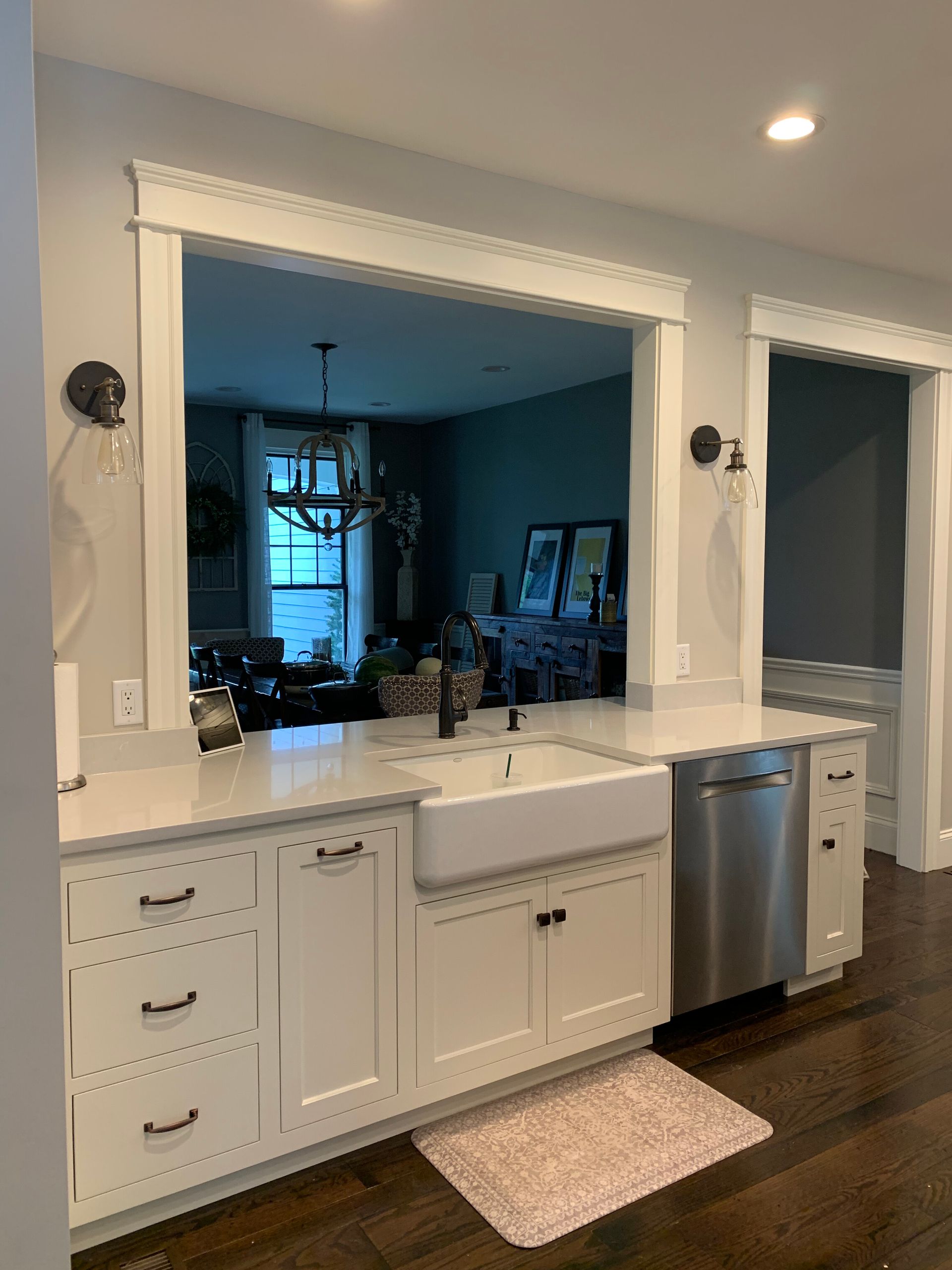 A white farmhouse-style kitchen sink and stainless steel dishwasher installed in a quartz countertop with white cabinetry.