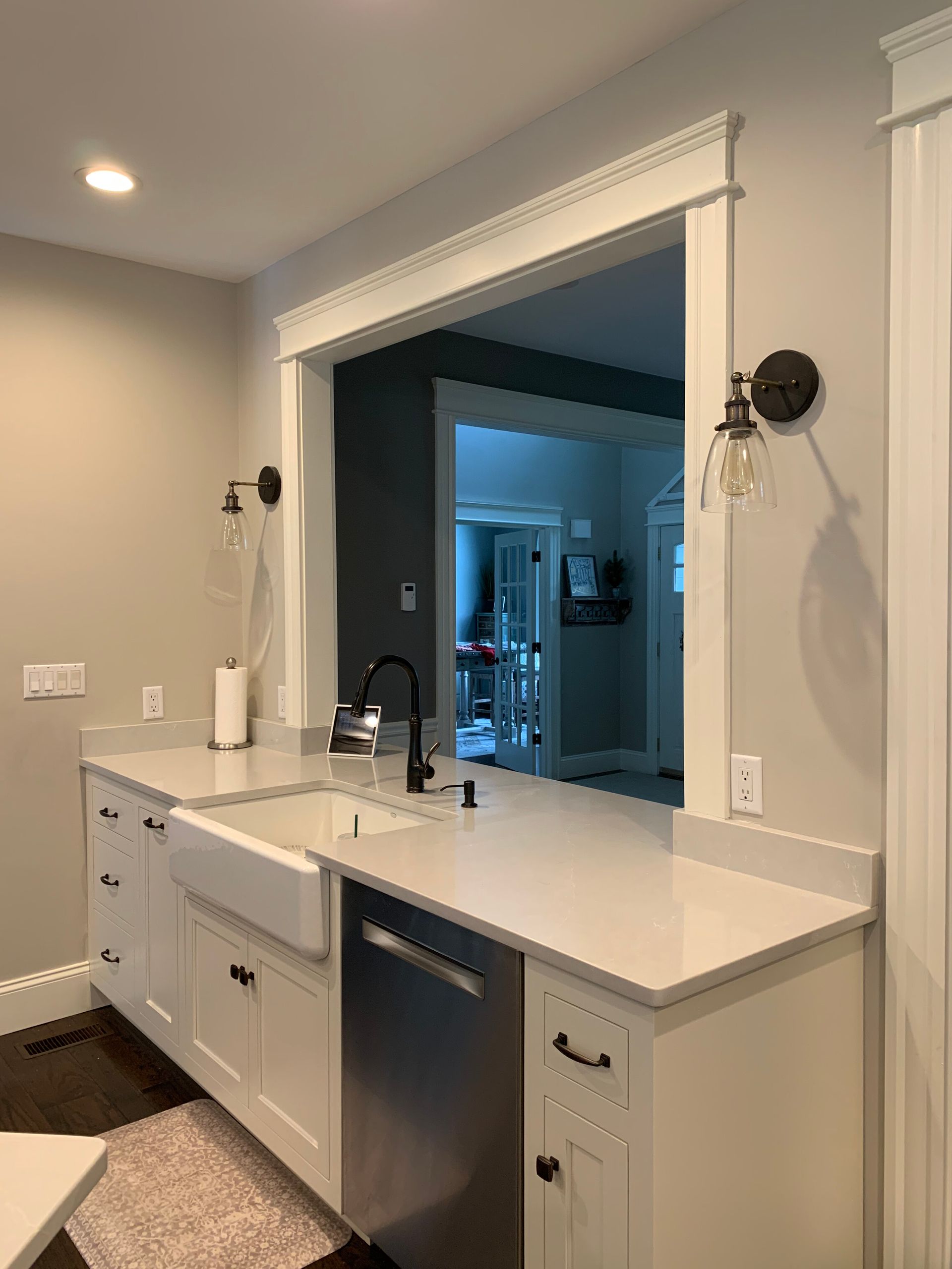 A white farmhouse sink and dishwasher in a kitchen with gray walls, white cabinets, and a decorative doorway pass-through.