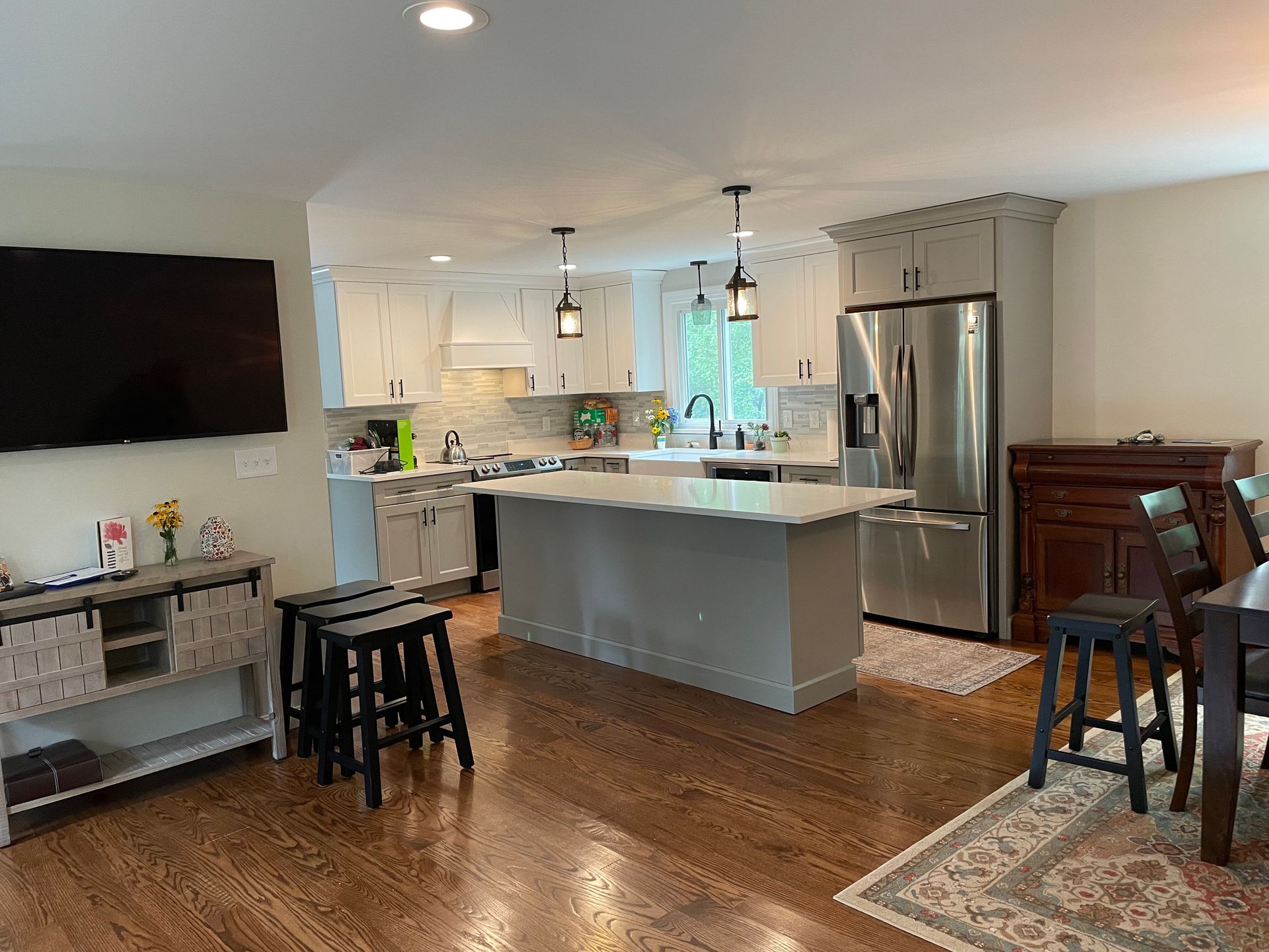 A kitchen with white cabinets, a light grey island, stainless steel appliances, and a wooden sideboard in an open room.
