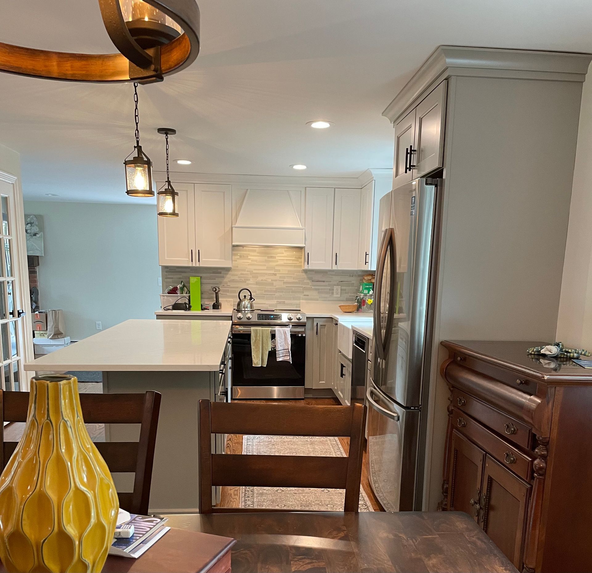 A kitchen features a white island, white cabinets, stainless steel appliances, and a warm-toned wood hutch in the foreground.