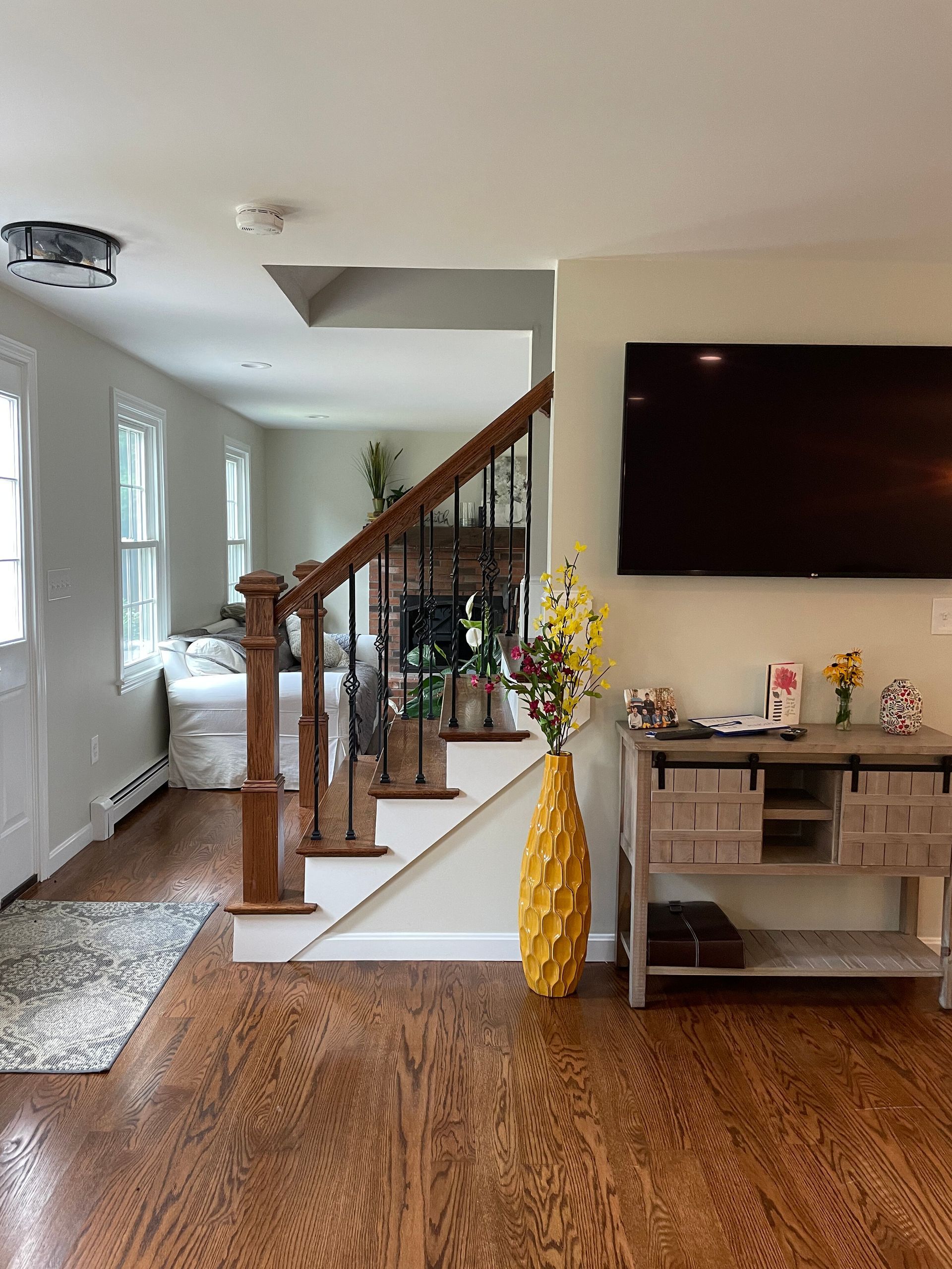 A staircase with wooden railings in a home interior, next to a console table with a yellow vase and a wall-mounted TV.