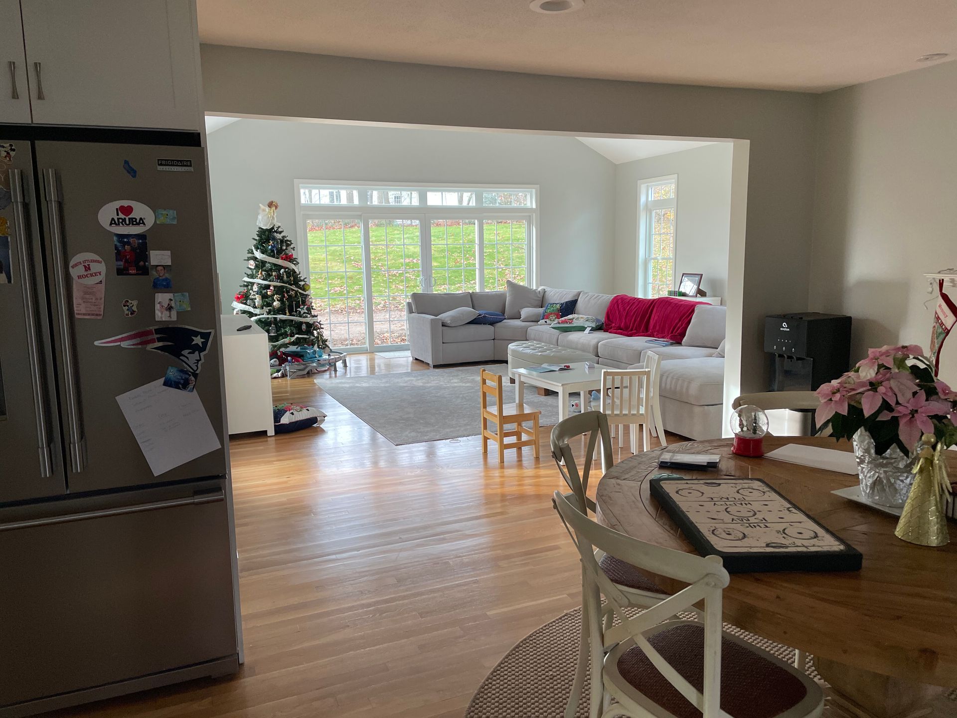 A bright open-concept living area with hardwood floors, a dining table, and a view into a living room with a Christmas tree.