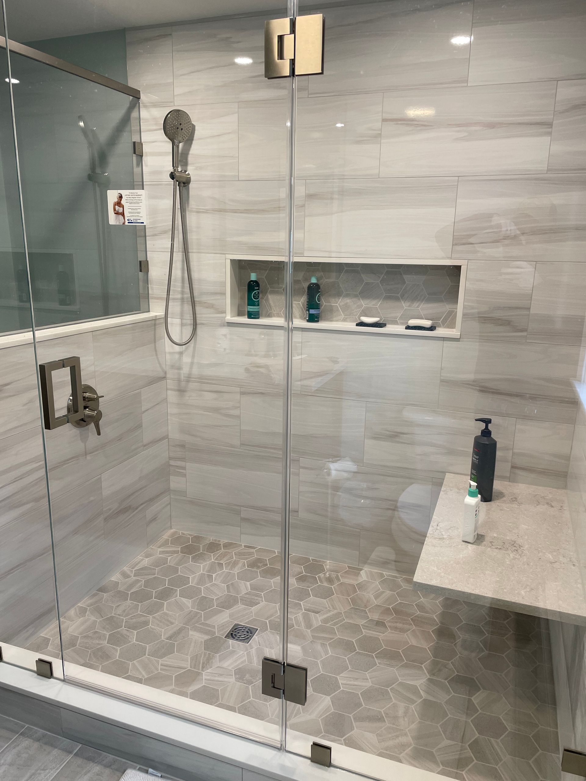 Modern walk-in shower with gray wood-look tile, built-in niche, floating seat, and glass door.