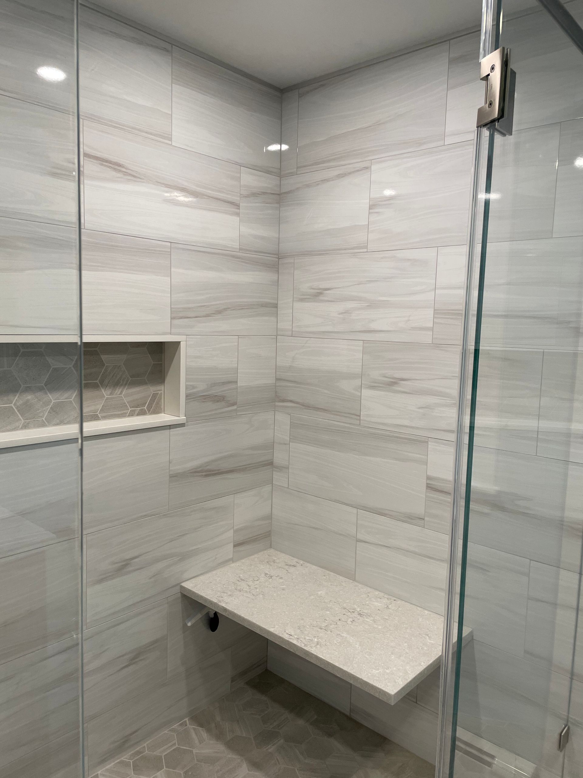 Modern shower with white marble-look tiles, a built-in stone bench, a recessed wall niche, and glass doors.