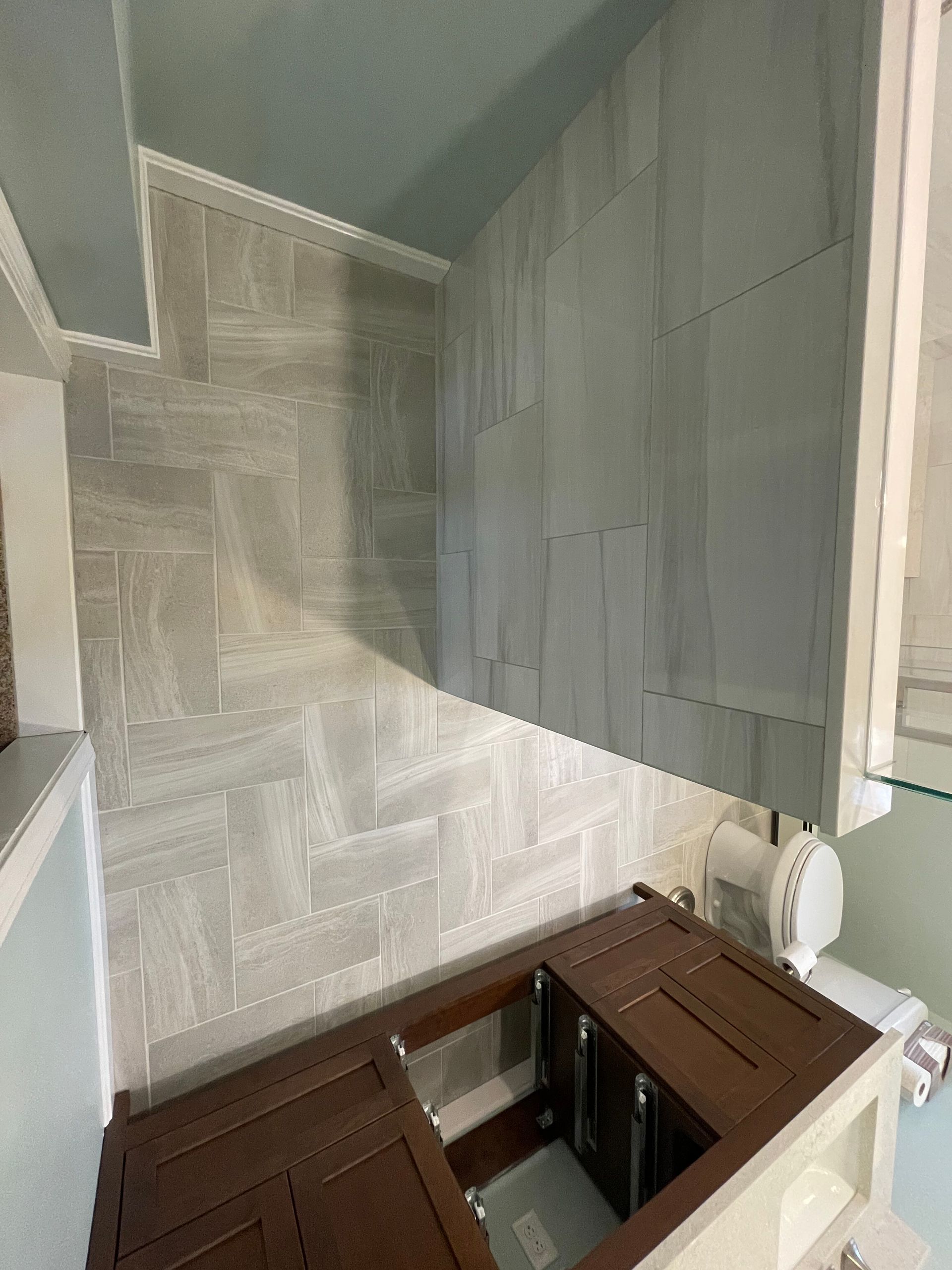 A bathroom under renovation, featuring a partially tiled herringbone wall and a dark wood vanity cabinet.