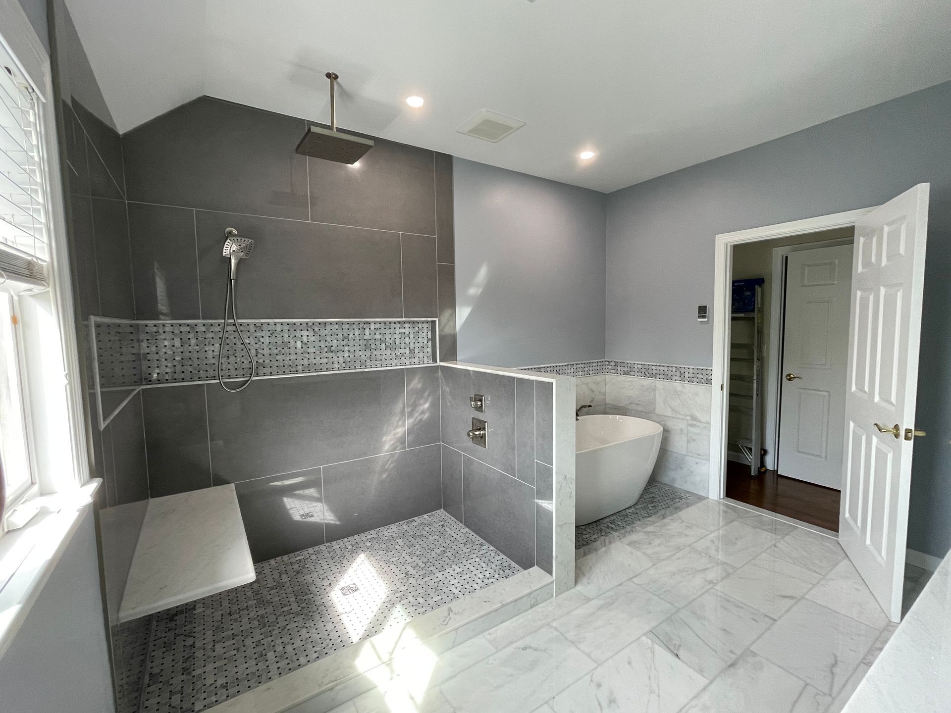 Modern bathroom featuring a gray-tiled walk-in shower with a rainfall head and a white freestanding tub.