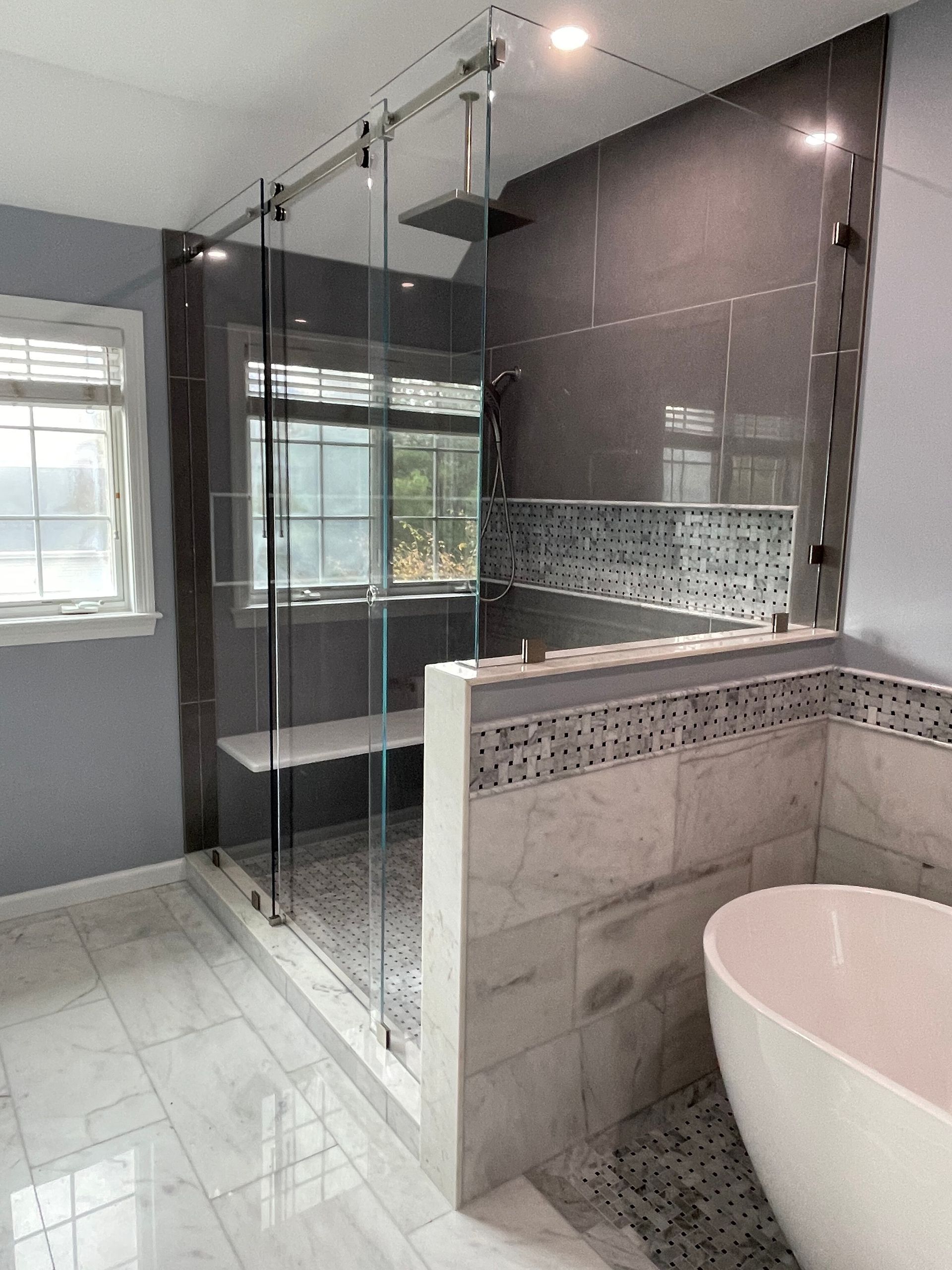 Modern bathroom featuring a glass shower enclosure with a bench, pebble-tiled floor, and a white freestanding bathtub.