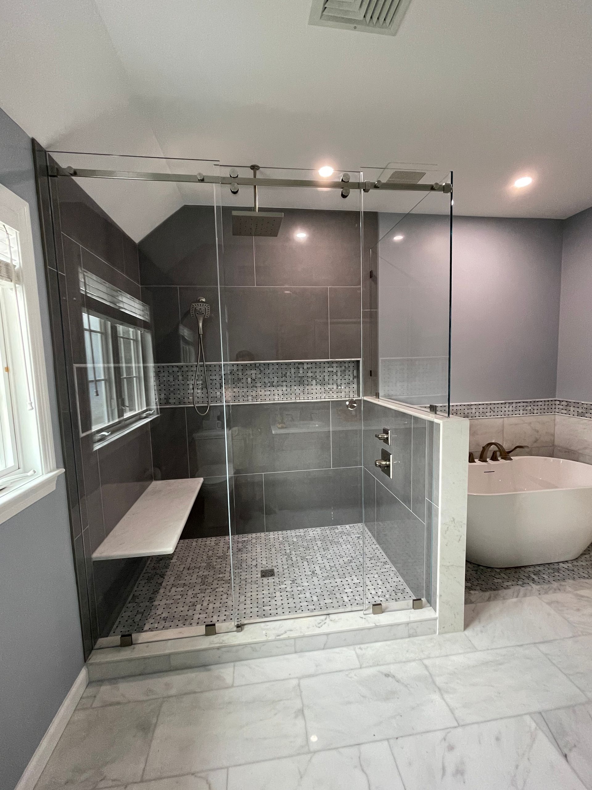 A modern bathroom featuring a walk-in glass shower with pebble flooring, a white bench, and a freestanding white bathtub.