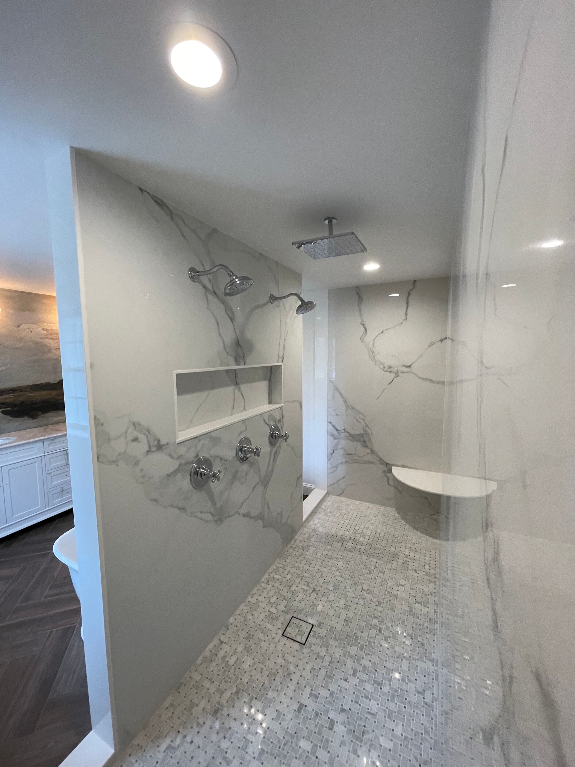 A modern, marble-tiled walk-in shower with a rain showerhead, a built-in bench, a recessed niche, and a pebble-tiled floor.