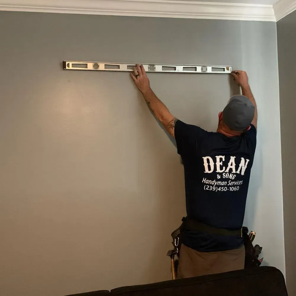 A man wearing a dean shirt measures a wall with a level