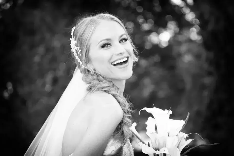 A black and white photo of a bride in a veil holding a bouquet of flowers.