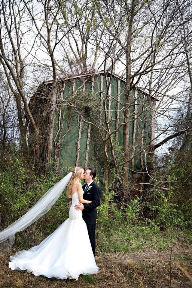 A bride and groom are kissing in front of a green building in the woods.