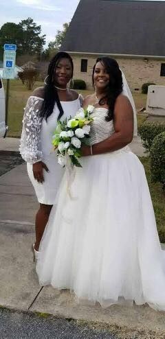 A woman in a white dress is standing next to a woman in a white dress holding a bouquet of flowers.