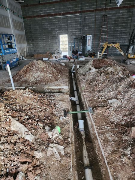 Construction site interior with excavator, trenches, and piles of dirt in a concrete building.