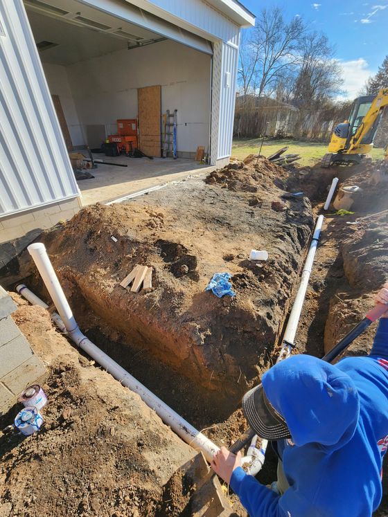 Person in blue hoodie digging a trench beside a garage with a shovel.