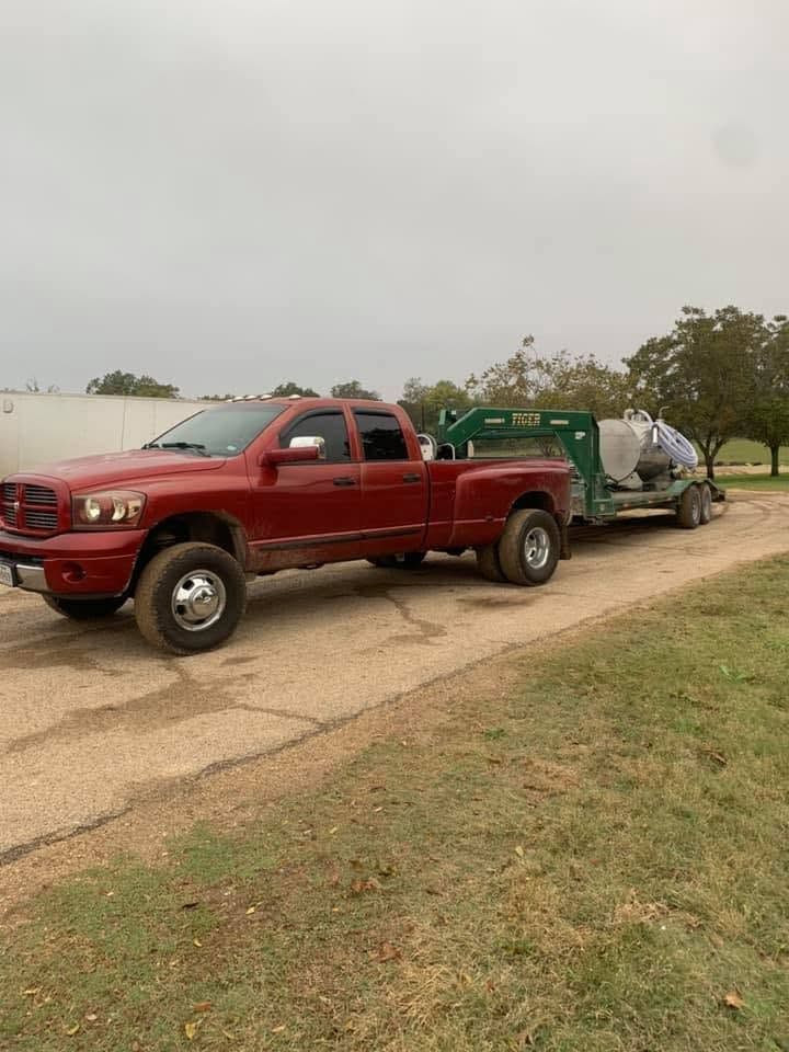 Red pickup truck towing a green trailer on a driveway in a grassy yard under cloudy skies