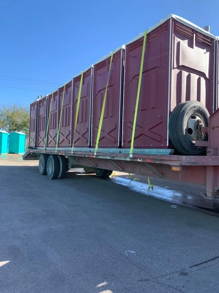 Maroon cargo trailer on a flatbed truck in a parking lot under a clear blue sky