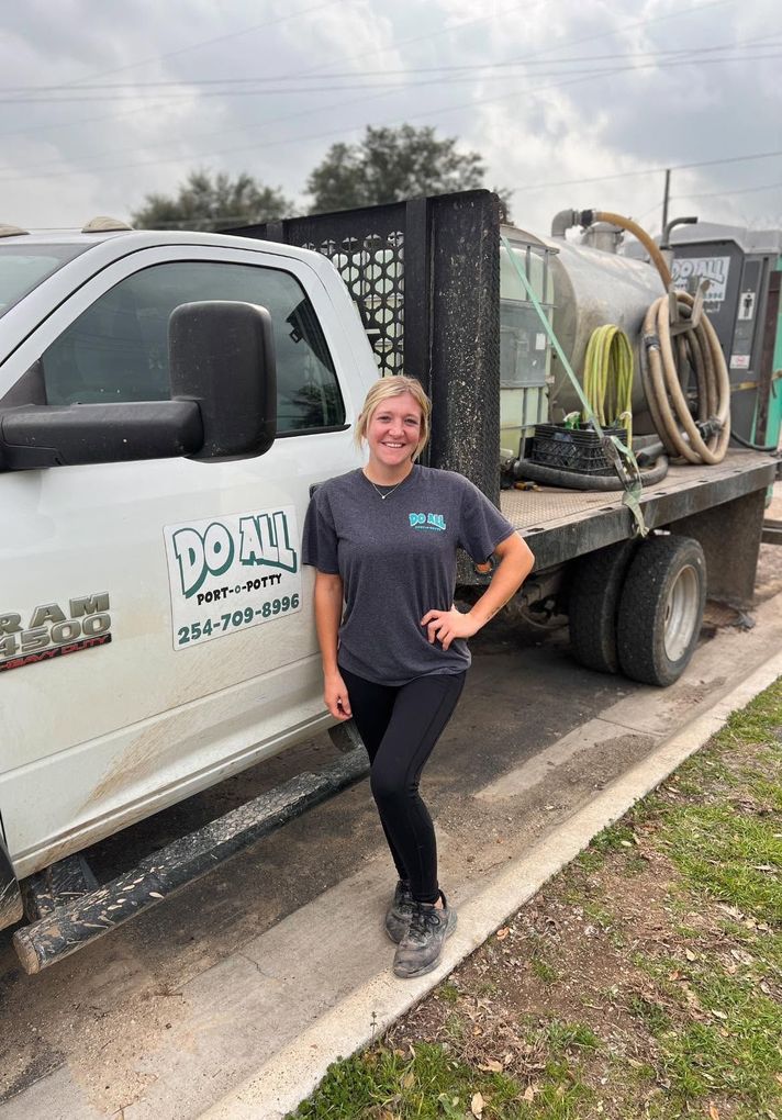 Woman standing beside a white work truck with landscaping equipment and hoses on the flatbed.