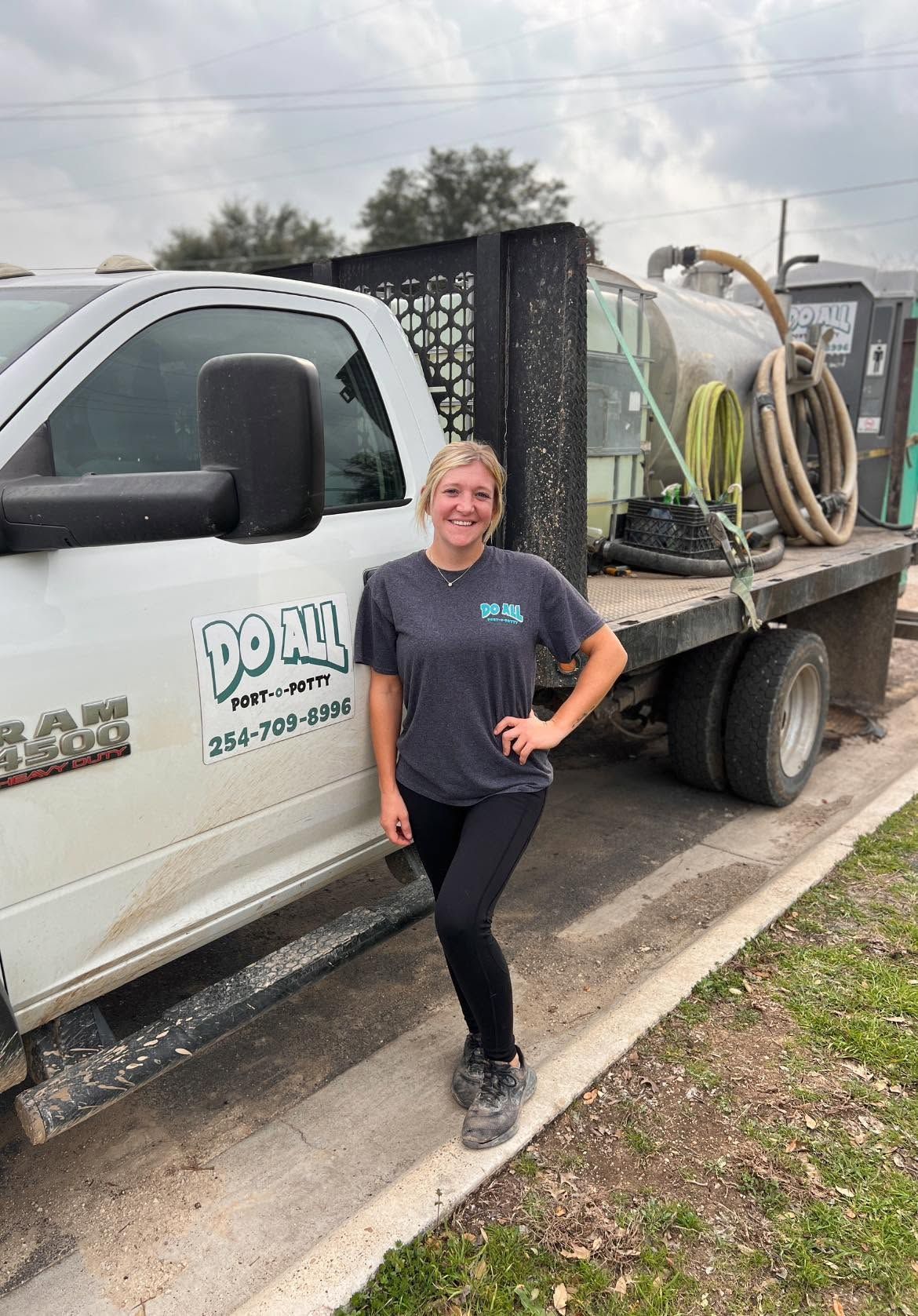 Woman standing beside a white work truck with landscaping equipment and hoses on the flatbed.