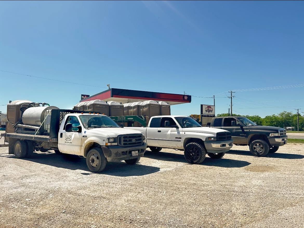 Three work trucks parked on a gravel lot beside a gas station under a clear blue sky.