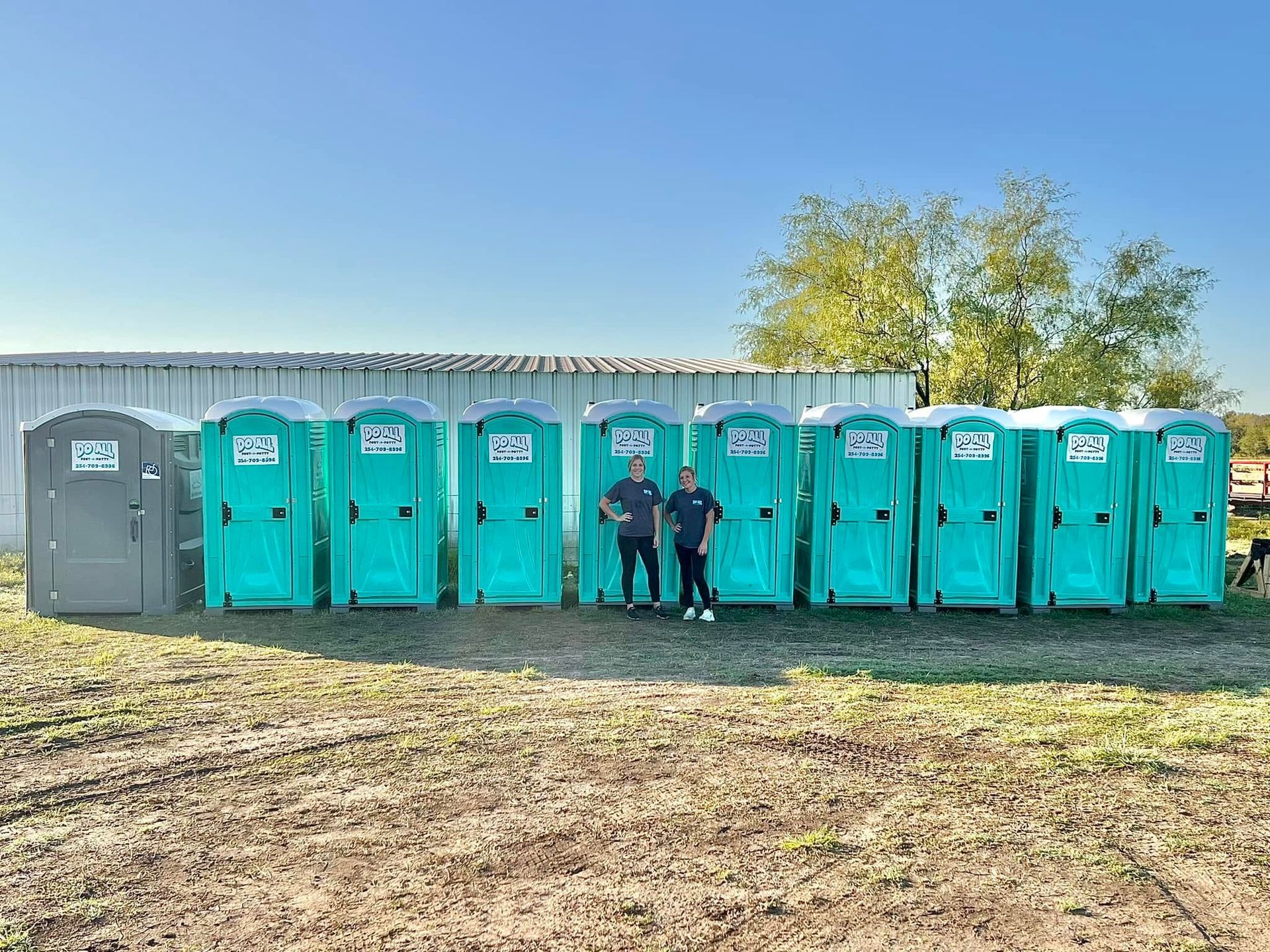 Row of portable toilets at an outdoor event, with two people standing in front.