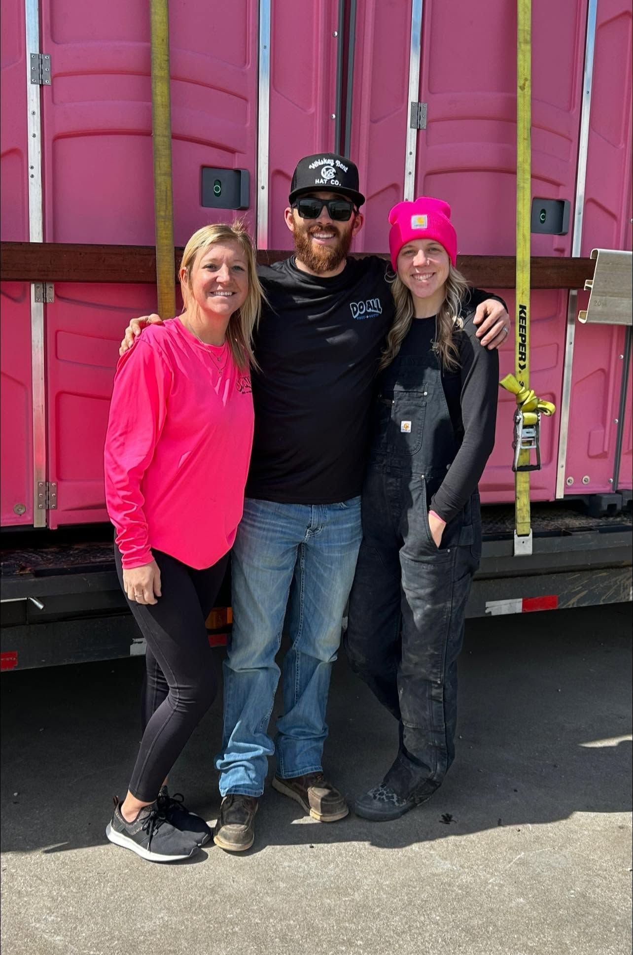 Three people standing together in front of a pink truck, smiling outdoors