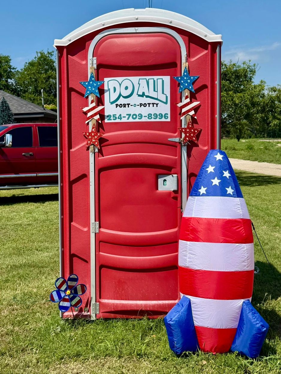 Red portable toilet with patriotic red, white, and blue rocket decoration on grass