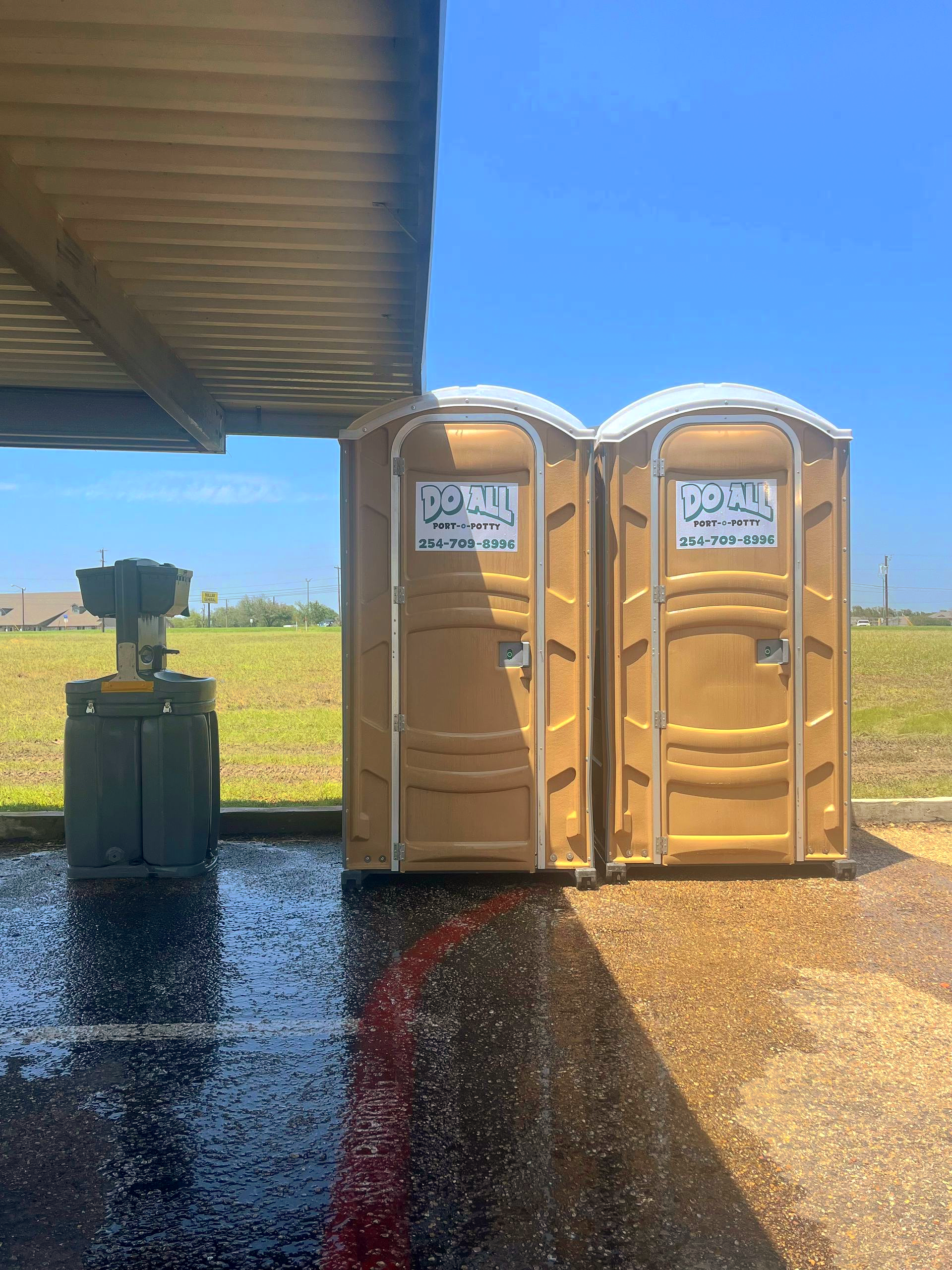 Two maroon portable toilets on a flatbed trailer under a clear blue sky