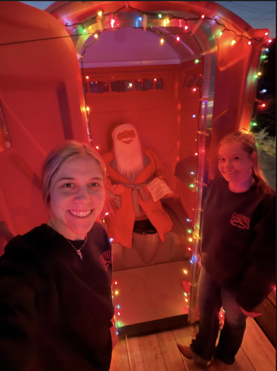 Two people posing beside a lit Santa display in a red holiday booth