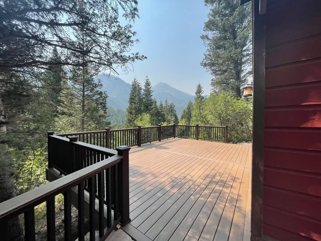 Wooden deck with black railings overlooking a forested mountain view in sunlight