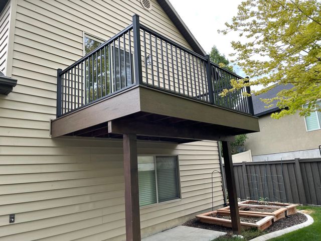 Back patio balcony with black railing over a beige house wall and a small fenced garden below