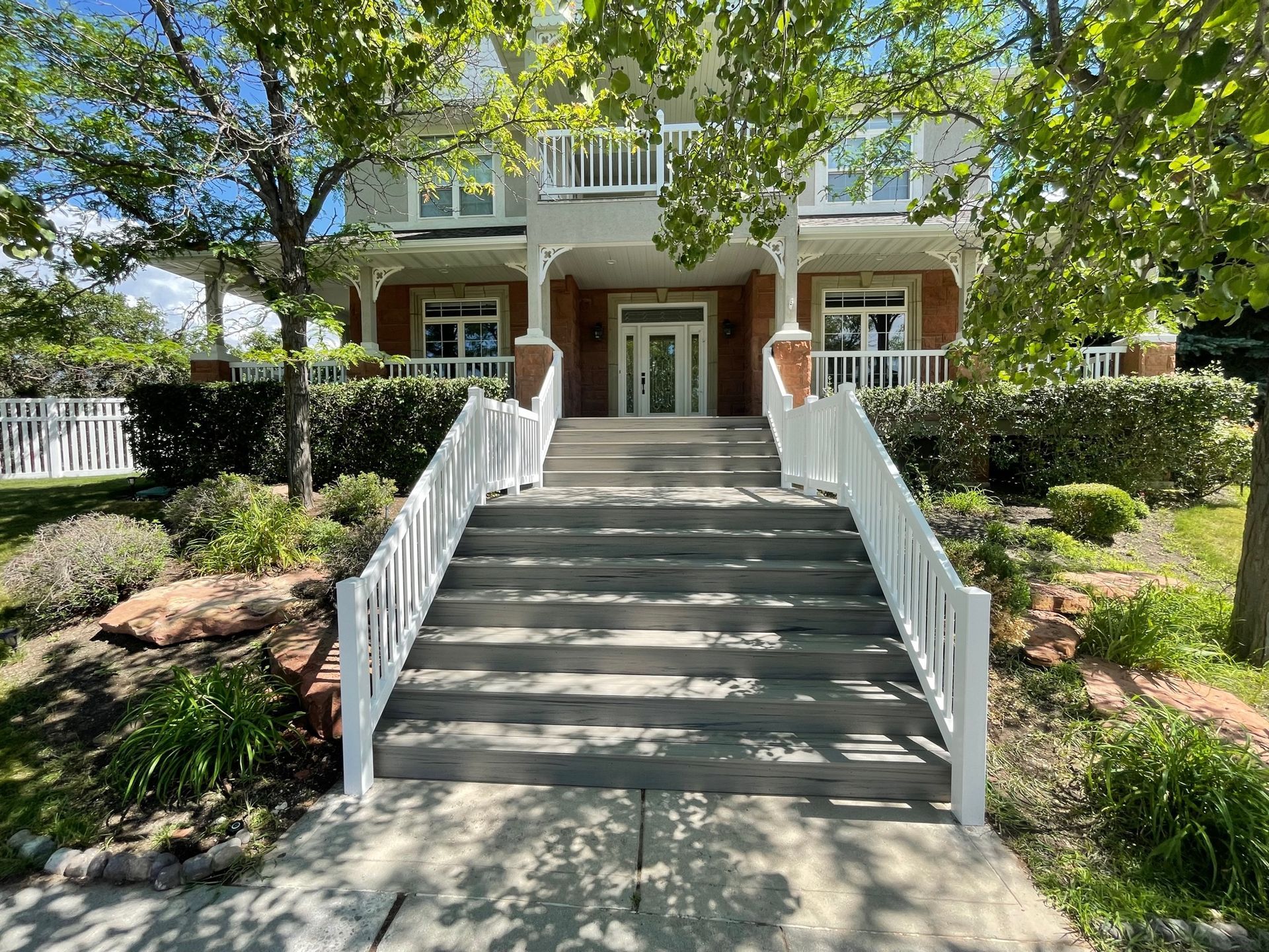 Front view of a large house with a wide staircase, white railings, and landscaped garden on both sides