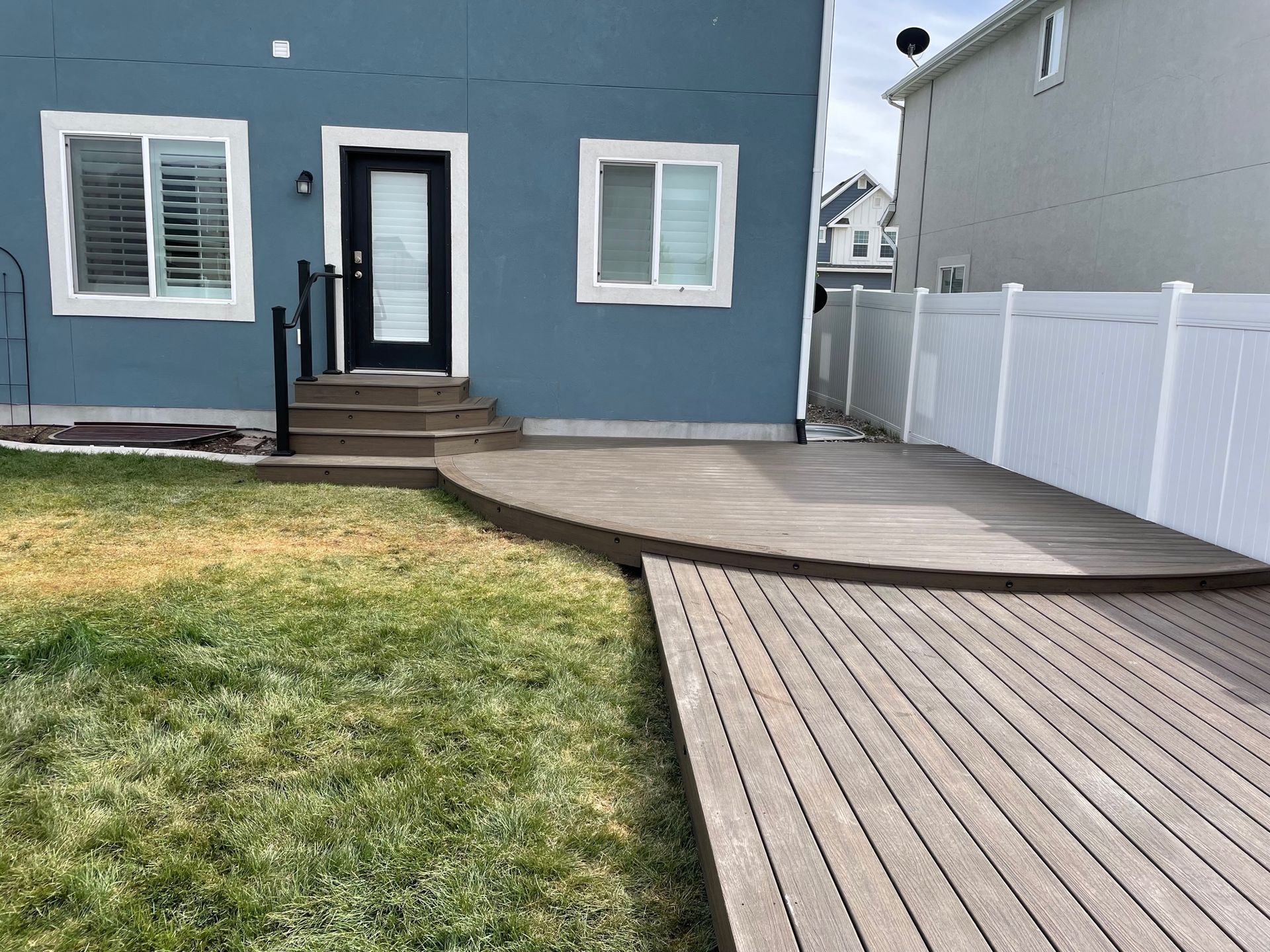 Backyard deck and walkway leading to a blue house with white trim and a white fence