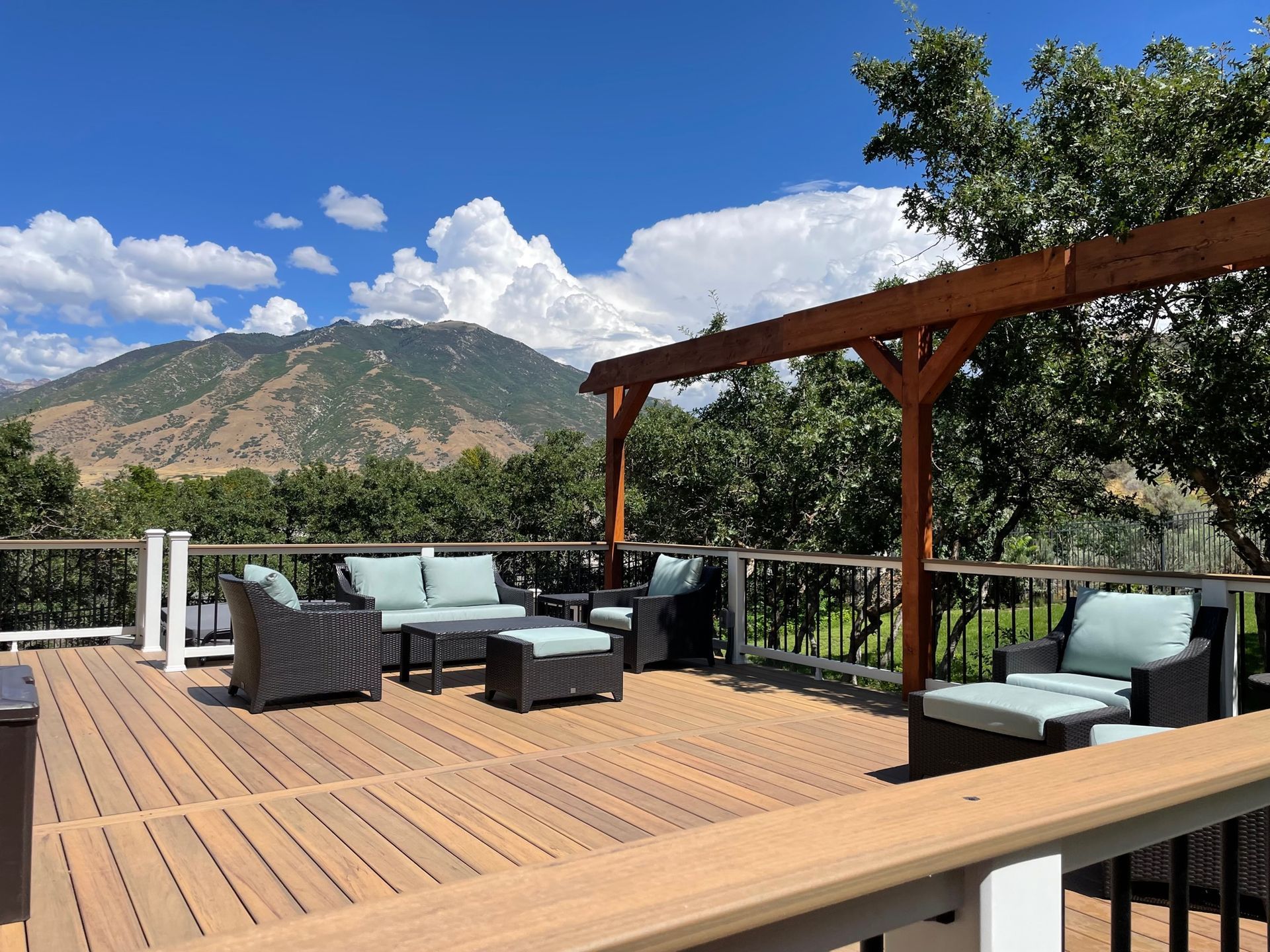 Sunny mountain-view deck with outdoor sofa, chairs, and a wooden pergola