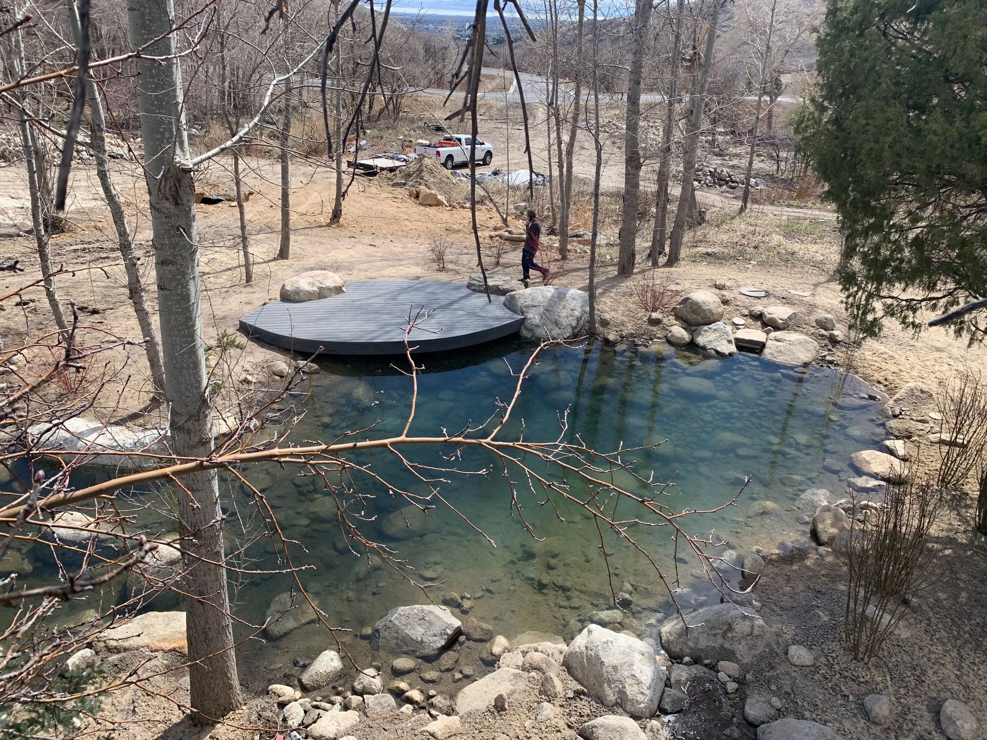 Small wooded pond with clear blue water, rocks, and a black round floating platform