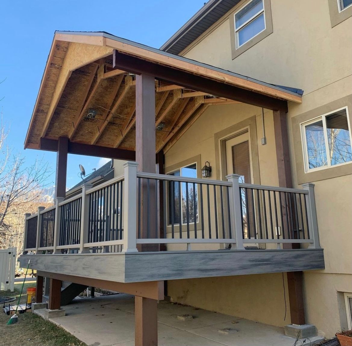 Covered wooden porch deck attached to a tan house, with railings and sloped roof