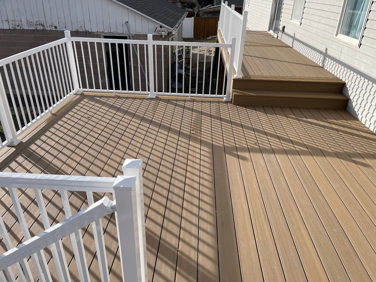 Wooden deck with white railing beside a house, with steps leading up to a doorway.
