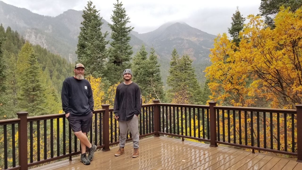 Two people on a wet wooden deck overlooking misty mountains and autumn trees