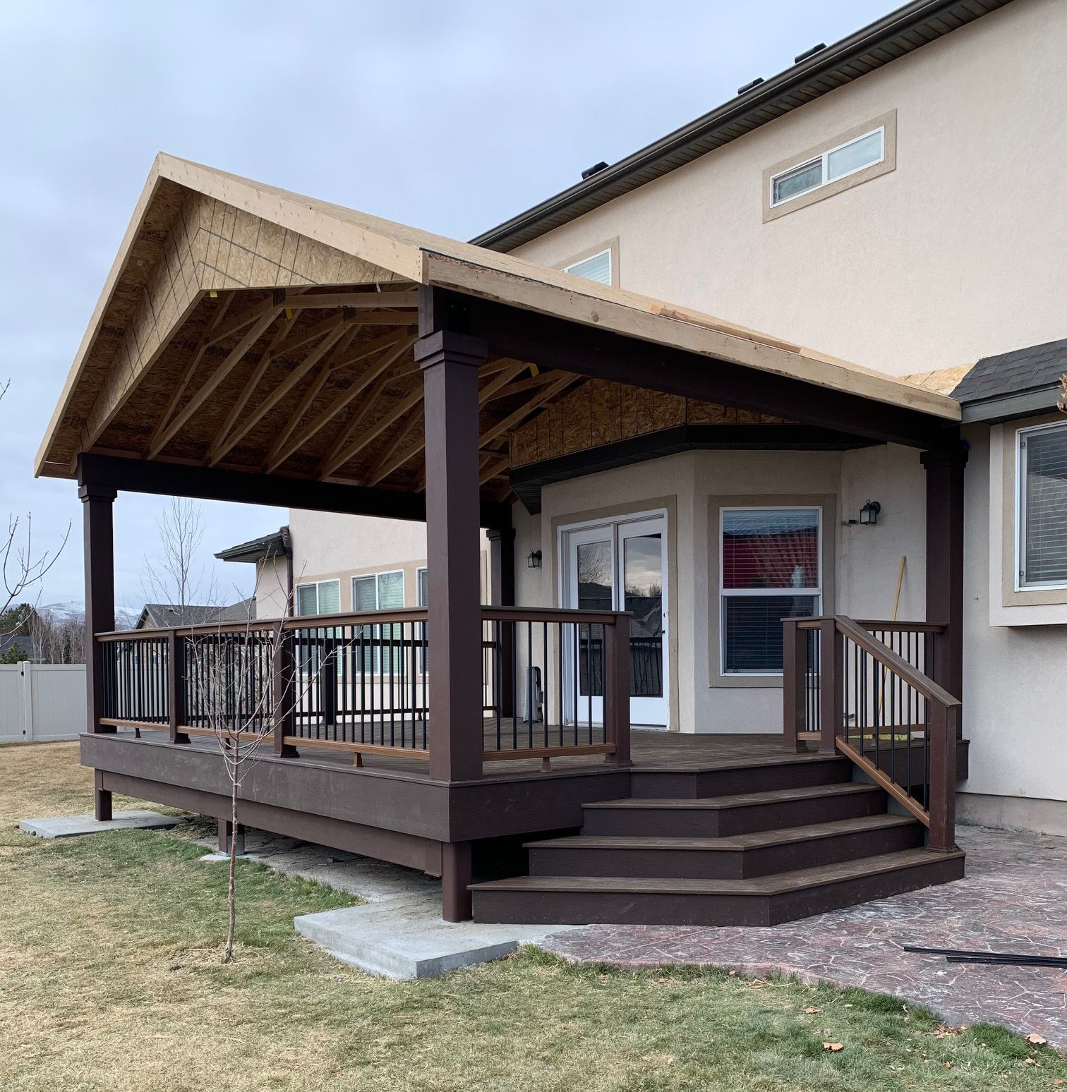 Covered wooden porch with steps and railing attached to a beige house